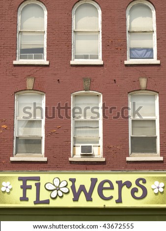 Green flower shop sign underneath six windows on a red brick building. Ontario, Canada.