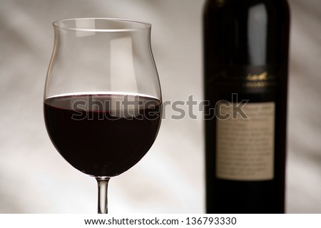 A large glass of red wine and a red wine bottle isolated on a textured grey background