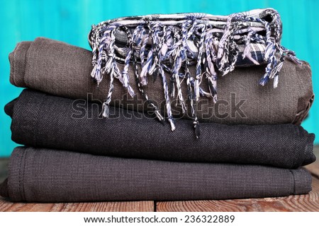 Stack of grey and black blue jeans with scarf on a wooden table with bright turquoise background
