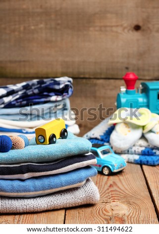 Still life and family concept. Stack of baby boy clothes with toys on a wooden table. Selective focus