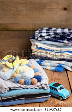 Still life and family concept. Stack of baby boy clothes with toys on a wooden table. Selective focus