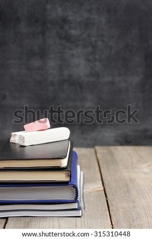 Still life, business, education concept. Notebook stack on a wooden table with chalk and chalkboard. Selective focus, copy space, school background