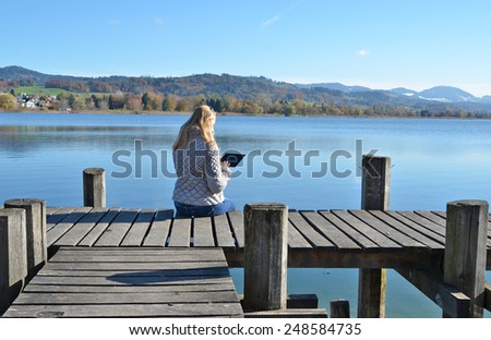 Girl reading from a tablet on the wooden jetty against a lake. Switzerland