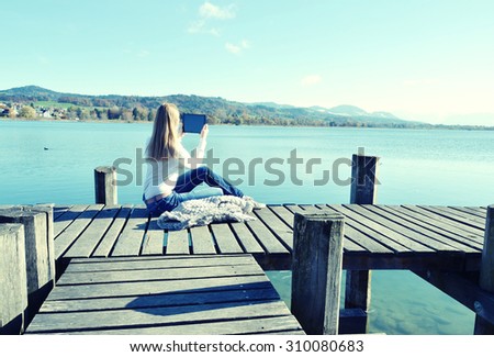 Girl reading from a tablet on the wooden jetty against a lake. Switzerland