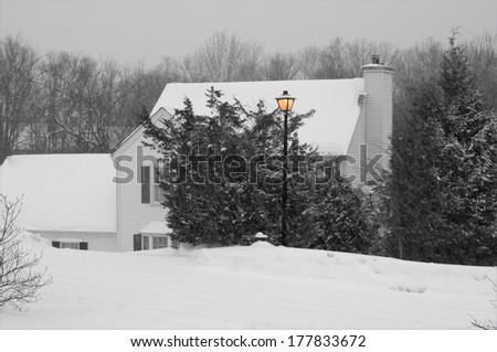 A black and white winter image with an orange lamp post in New England during a snow storm.
