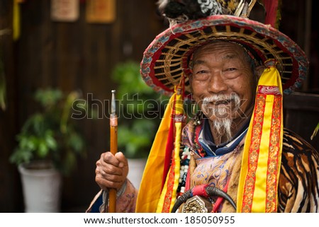 LIJIANG, CHINA - MARCH 30, 2014: A Naxi nationality old man dressed in ancient Dongba clothing, smiling and welcome the travelers. Located in Lijiang Ancient City, Yunnan Province, China.