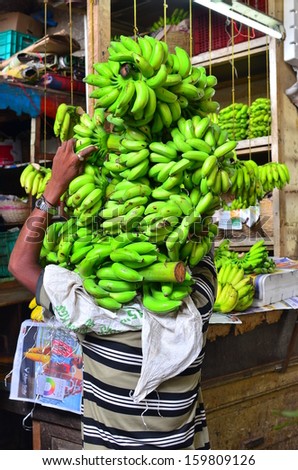 Mumbai, India - circa October 2013 - A man carrying big bunches of green bananas over his shoulder at the local Crawford market