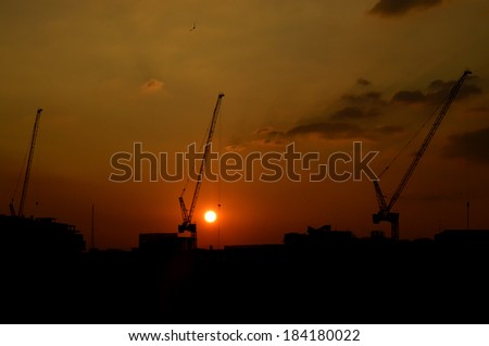 Silhouette construction cranes on top of under construction site at sunset