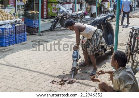 Mumbai, India - August 22, 2014 - Worker drilling concrete ground using electric hammer at local market
