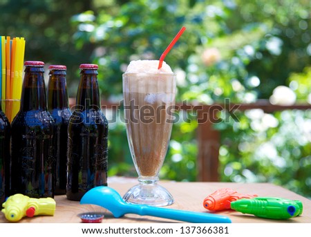 Root beer float outdoors with ice cream scoop, straws, squirt guns and bottles
