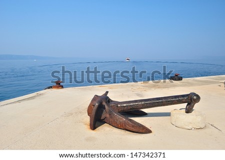 Old rusty ship anchor on port with departing ship in background