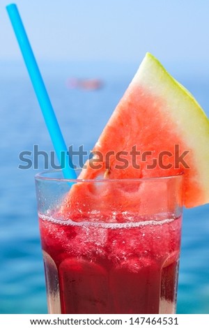 Fresh tropical fruit cocktail with water melon slice on a beach. Blurred sea on background. Vertical image.