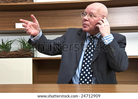 A company director talking on his mobile telephone, and at the same time, seeking to attract a staff member\'s attention in the next office cubicle.