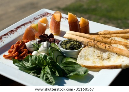 An Antipasto platter containing Semi-dried Tomatoes, Baby Bocconcini, Prosciutto-wrapped Rockmelon, Black Olives, and Sour Dough