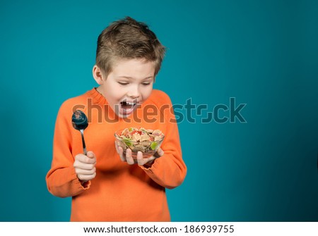 Cute boy eating cereals isolated on blue background.