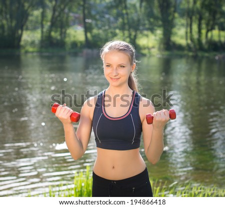 Fitness exercise. Woman using dumbbells in fitness strength training workout outside in the park. Instructor exercising with small weights near the river.