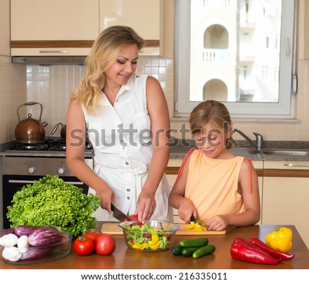 Young woman and girl making fresh vegetable salad. Healthy domestic food concept. Mother and daughter cooking together, help children to parents.