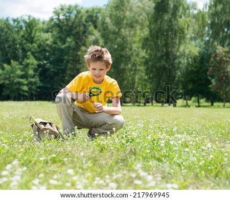 Happy boy enjoying sunny summer or autumn day in nature on green grass. Kid with magnifying glass outdoors.