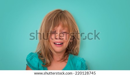 Little girl with sad expression and tears. Crying child on turquoise background. Emotions.