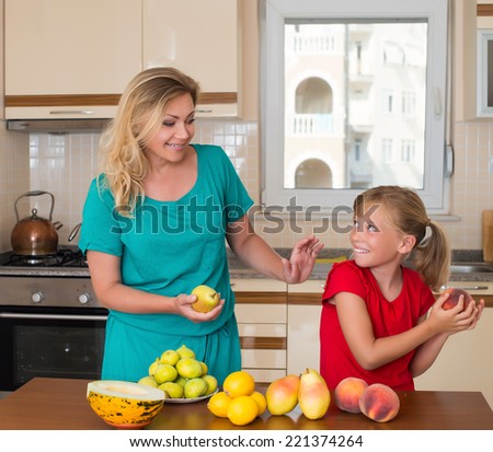 Smiley mother with her keeping sweet pear daughter. Healthy eating - woman and child in the kitchen with different kinds of fruits for breakfast food