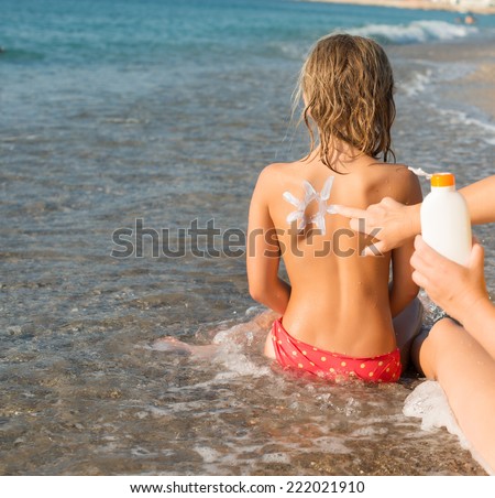 Mother putting suncream on her daughter. Sun protection. Sun on her back made with suncream.
