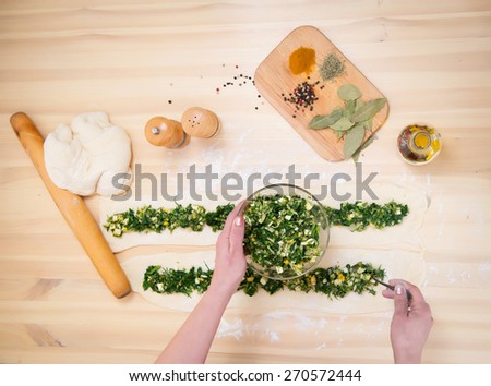 Preparing pie with spinach and feta cheese, food. Cooking pie with green stuffed spinach, eggs and cheese close up on wooden table. Top view.