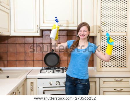 Happy woman cleaning kitchen. Beautiful girl with cleaning spray wearing protective gloves showing muscular strength.