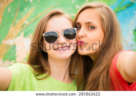 Closeup portrait of two teenage girls friends in hipster outfit having fun kissing and taking a selfie. Outdoors, lifestyle, fun.