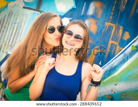 Stylish lifestyle urban portrait of two pretty best friends girls. Having fun, kiss and say hello. Two funny affectionate women friends laughing and kissing outdoors.