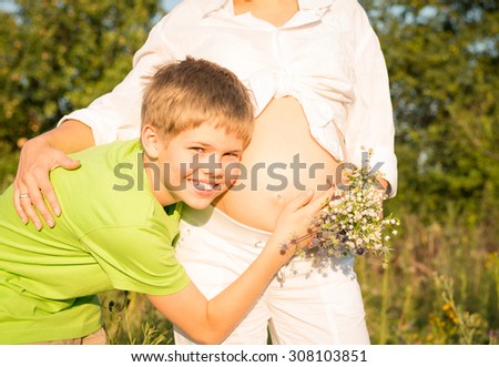 Portrait of happy boy holding listens belly of pregnant woman. Mothers day concept.