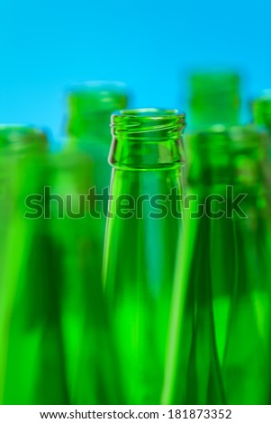 Seven green bottle necks on blue background, in center one bottle in focus.