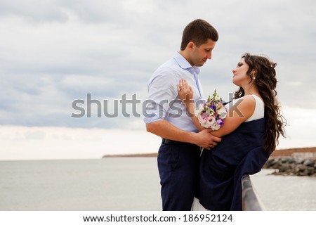 Gentle bride and handsome groom standing on the pier. Happy newlyweds on the beach.