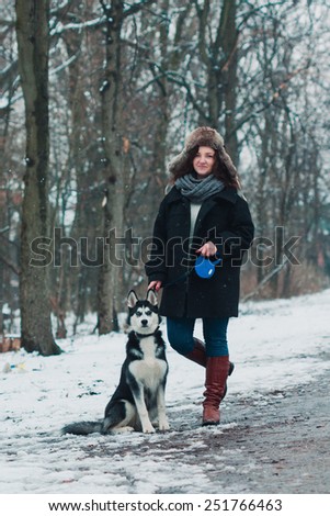 Young woman with husky dog in the winter park. Snow is falling in the forest.