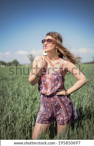 Beautiful fashion hippie woman posing in a wheat field wearing a boho jumpsuit romper, with the wind blowing in her blonde hair