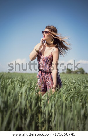 Beautiful fashion hippie woman in a wheat field wearing a boho jumpsuit romper, with the wind blowing in her blonde hair