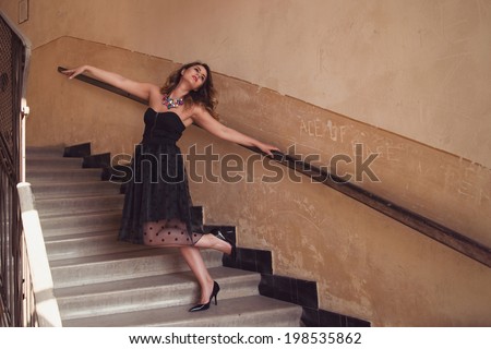 Beautiful elegant attractive woman posing on old palace stairs wearing a veil skirt with dots and a black top corset with front zipper, holding on the railing with one hand and lifting the other