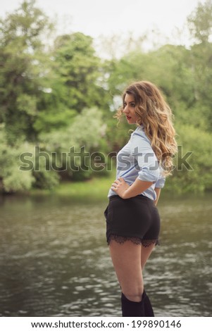 Beautiful Woman at a river side posing with her back wearing sexy shorts, black with lace and over knee boots