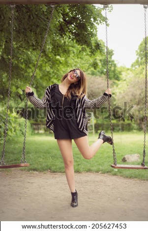 Fashion shoot of sexy woman posing playful between swings outdoor in a black romper jumpsuit