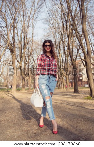 Fashion model wearing ripped jeans posing outdoor with her legs crossed holding a big white bag