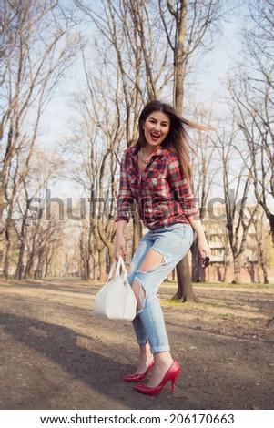 Fashion model wearing sexy ripped jeans posing bended and happy outdoor on red high heels