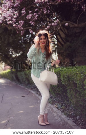 Fashion shoot of pretty woman wearing sexy white pants and turquoise polka dots shirt posing outdoor in a Spring Background with flowers