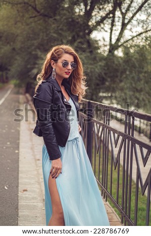 Gorgeous blonde posing playful in a sexy light blue dress tight and fluid on her body. Fashion close up portrait of beautiful woman at the river side