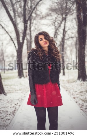 Fashion shoot while snowing of attractive blonde in a romantic look, red dress, black fur and sexy tights