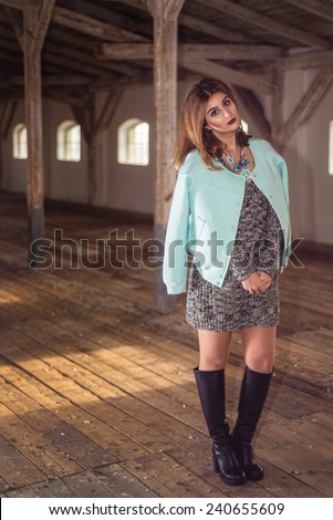 Fashion woman wearing baby blue baseball jacket over sexy knitted dress. Model posing in old attic with over-knee boots