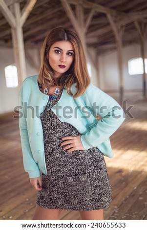 Fashion woman wearing baby blue baseball jacket over sexy knitted dress. Model posing in old attic