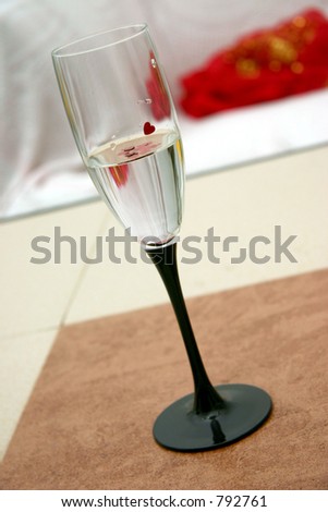 A flute wine-glass with clear liquid and tiny red heart floating on its surface