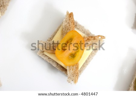 Yellow cherry tomato with a slice of cheese canapé, top view