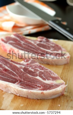 Two large cuts of raw Australian lamb cuts on a wooden chopping board in kitchen