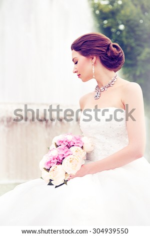 Beautiful bride with pretty bouquet sitting in front of the fountain.