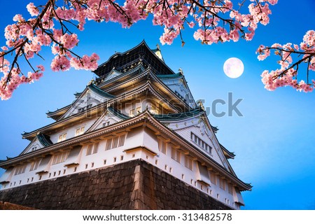 Japan. Beautiful night view of Osaka castle with cherry blossom and moon. Oriental beauty scene.